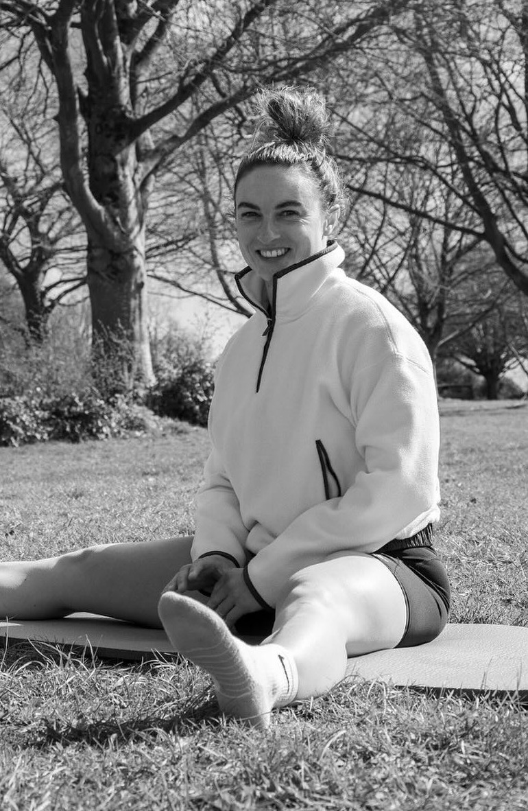 Kizzy Hunt, APPI Pilates instructor and personal trainer, sitting on a mat outdoors